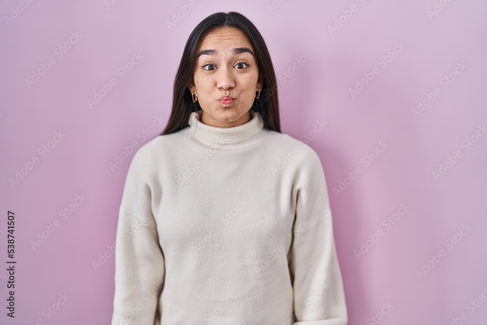 Young south asian woman standing over pink background puffing cheeks with funny face. mouth inflated with air, crazy expression. Young south asian woman standing over pink background puffing cheeks with funny face. mouth inflated with air, crazy expression.