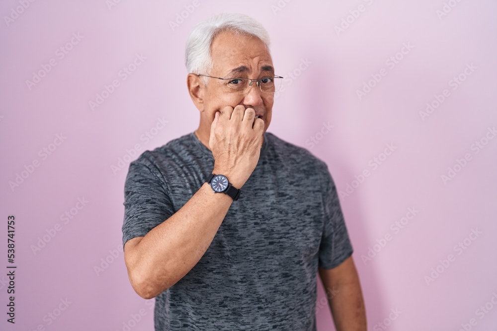 Middle age man with grey hair standing over pink background looking stressed and nervous with hands on mouth biting nails. anxiety problem. Middle age man with grey hair standing over pink background looking stressed and nervous with hands on mouth biting nails. anxiety problem.