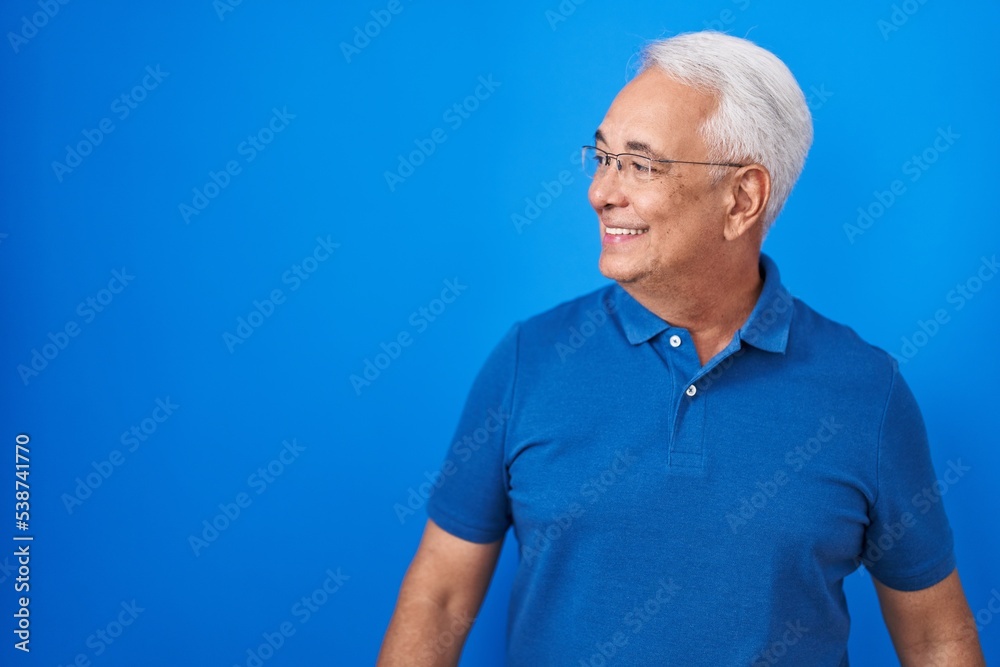 Middle age man with grey hair standing over blue background looking away to side with smile on face, natural expression. laughing confident. Middle age man with grey hair standing over blue background looking away to side with smile on face, natural expression. laughing confident.