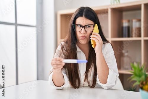 Young brunette woman holding pregnancy test result speaking on the phone depressed and worry for distress  crying angry and afraid. sad expression.