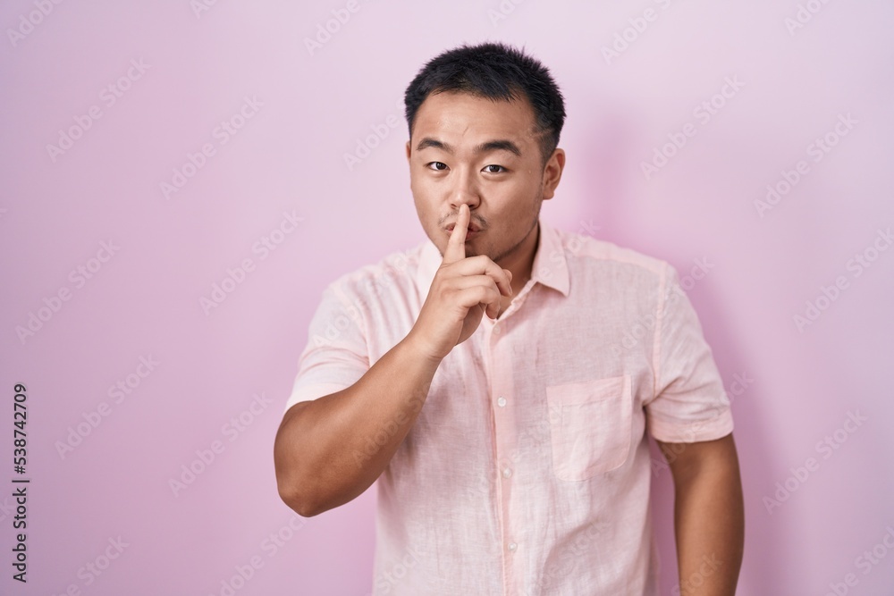 Chinese young man standing over pink background asking to be quiet with finger on lips. silence and secret concept. Chinese young man standing over pink background asking to be quiet with finger on lips. silence and secret concept.