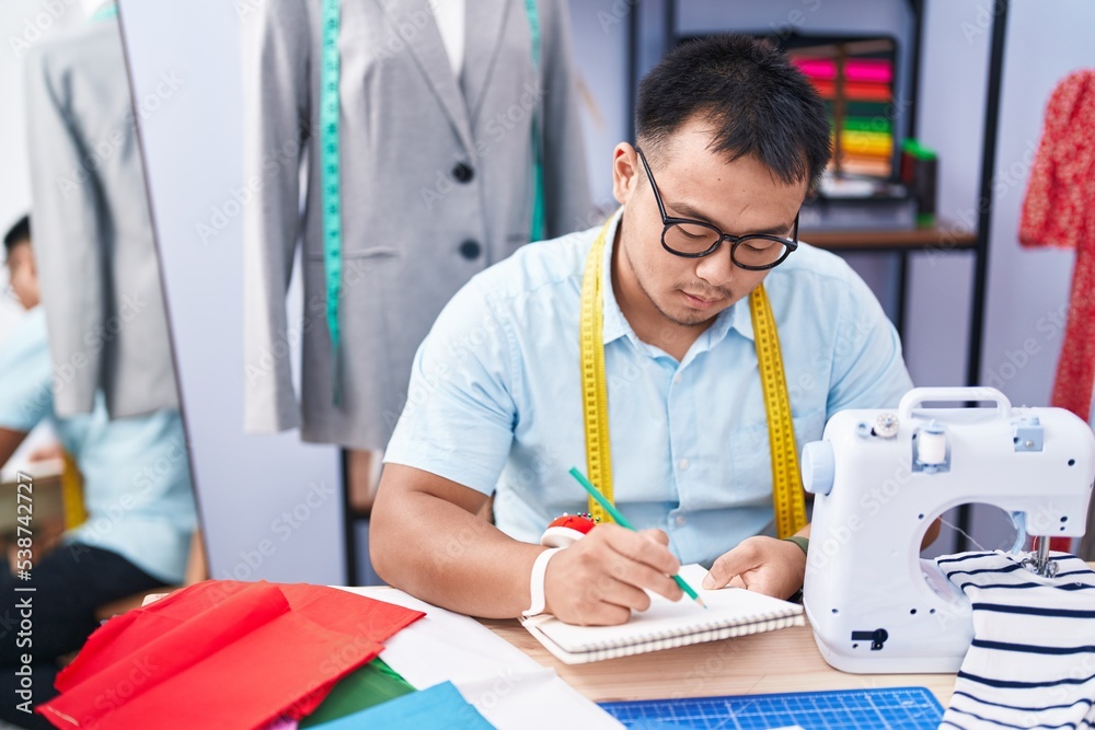 Young chinese man tailor drawing on notebook at tailor shop