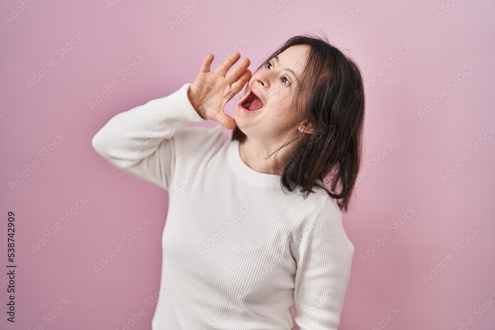 Woman with down syndrome standing over pink background shouting and screaming loud to side with hand on mouth. communication concept. Woman with down syndrome standing over pink background shouting and screaming loud to side with hand on mouth. communication concept.