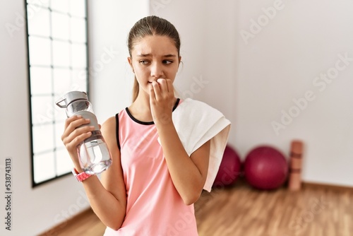 Young brunette teenager wearing sportswear holding water bottle looking stressed and nervous with hands on mouth biting nails. anxiety problem. photo