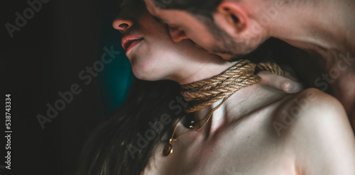 A young, slim, naked hot woman with knots of natural ropes kissed by her boyfriend. Ancient Japanese art of aesthetic bondage and tying shibari kinbaku. Concept of BDSM sex games.