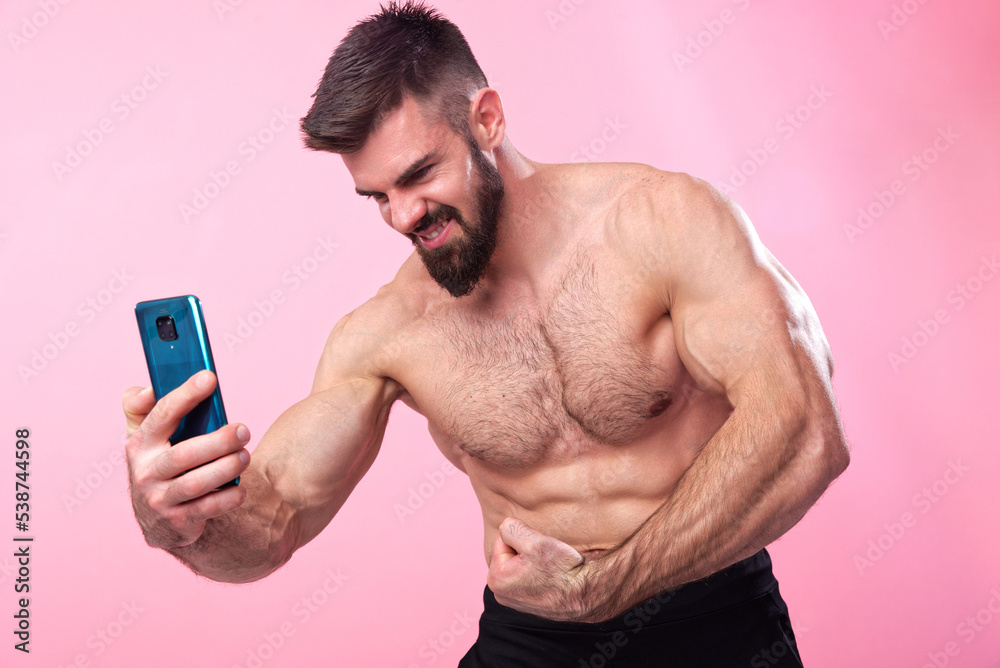 Strong and muscled bodybuilder taking a selfie with his smartphone of his shirtless torso, showing off his gains to friends on social media Strong and muscled bodybuilder taking a selfie with his smartphone of his shirtless torso, showing off his gains to friends on social media