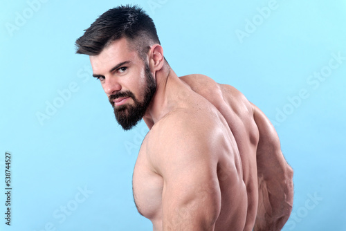 Young happy bodybuilder posing from the back, showing his back muscles and looking over his shoulders