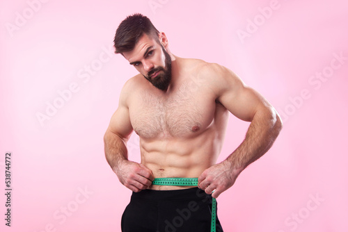 Fotografie Strong bodybuilder measuring the width of his waist, putting a measuring tape ov