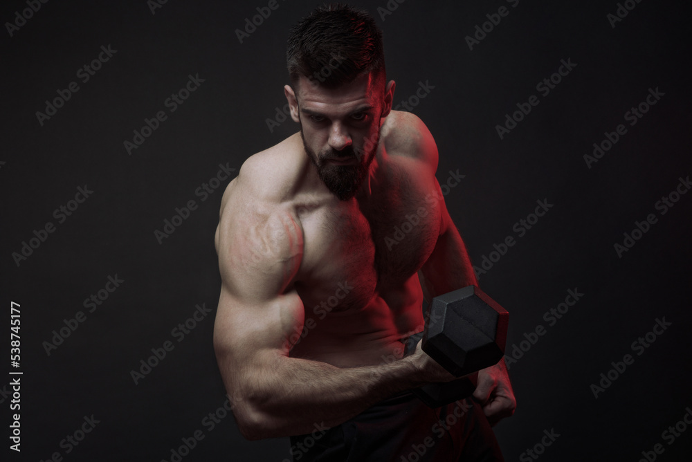 Young shirtless bodybuilder lifting a heavy dumbbell, studio image, dark background, dramatic atmosphere