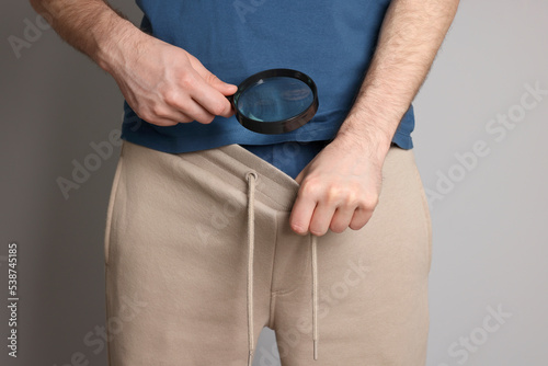 Man examining genital herpes with magnifying glass on beige background, closeup. photo