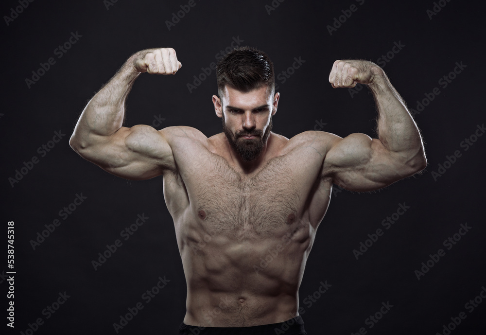 Beast mode - strong shirtless man, a bodybuilder, flexing his biceps, showing off his big arms and muscular body, dark image, black background