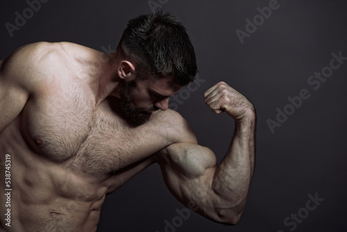 Young shirtless man, a bodybuilder, flexing his biceps, showing off his big arms Fototapet