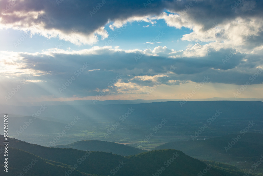 Rays of light shine down from a cloudy but blue sky onto the rural Shenandoah Valley as seen from Skyline Drive inside Shenandoah National Park, Virginia.