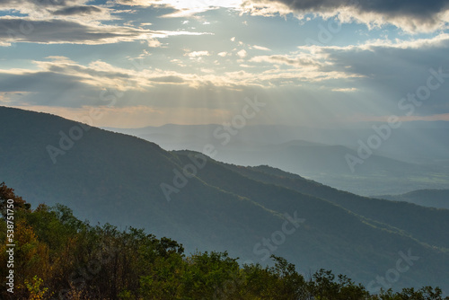 Rays of light shine down from a cloudy but blue sky onto the sides of the Blue Ridge Mountains as seen from Skyline Drive inside Shenandoah National Park, Virginia. © Pábitel Photography