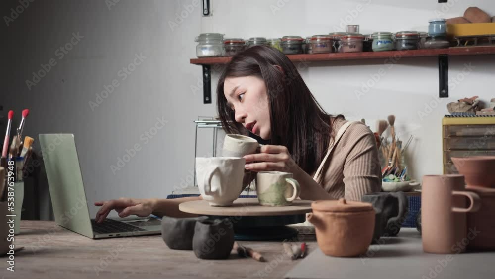 Young woman using smartphone and receive orders clay ceramic from customer. Woman typing keyboard on laptop computer for real time sell in business. Concept of business, technology and logistic. Young woman using smartphone and receive orders clay ceramic from customer. Woman typing keyboard on laptop computer for real time sell in business. Concept of business, technology and logistic.