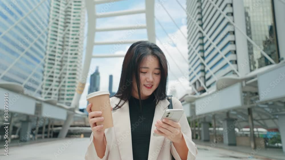 A business woman walking ,looking at smartphone and holding a coffee cup on city street A business woman walking ,looking at smartphone and holding a coffee cup on city street