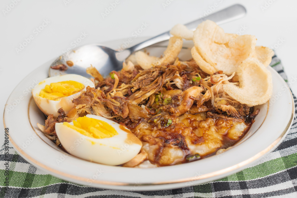 chicken porridge or bubur ayam. Asian style of chicken porridge. topped with shredded chicken, egg and crackers on white bowl and tablecloth. Isolated on white background