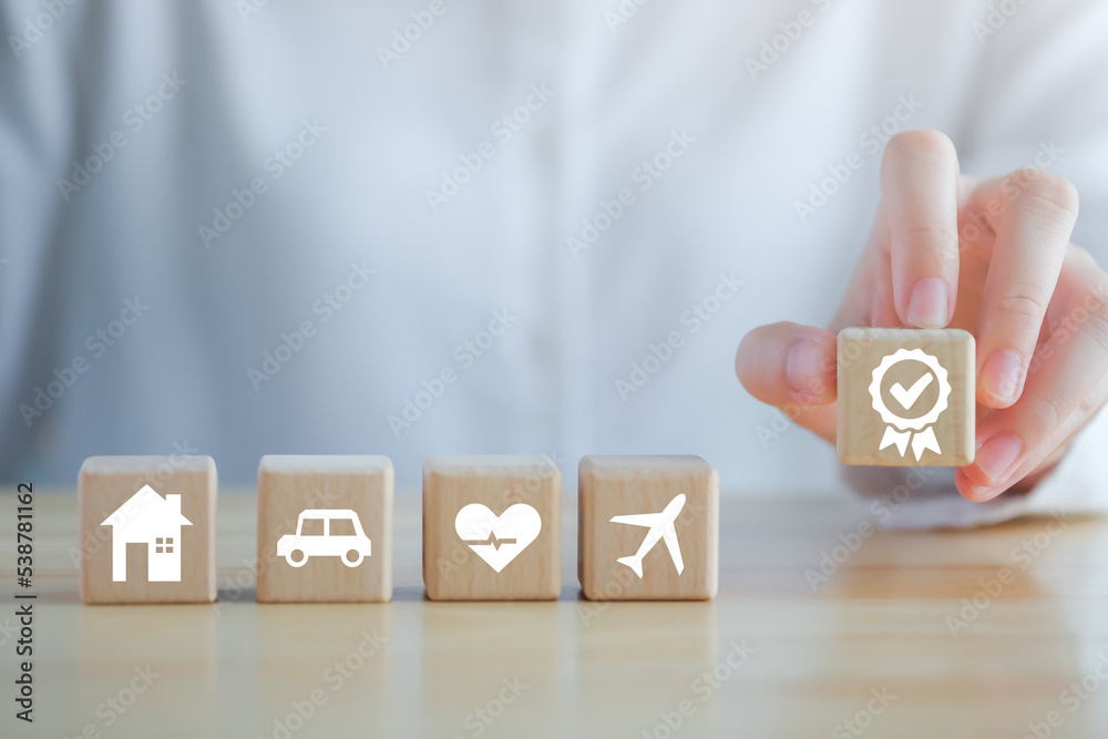Naklejka premium Insurance concept. Protection against a possible eventuality. Hand holding quality assurance with House, Car, healthcare and travel icon on wood block for Warranty security and assurance life concept.