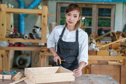 portrait of beautiful asian woman carpenter dealing with handicraft, woman has own business connected with making wooden furniture in workshop