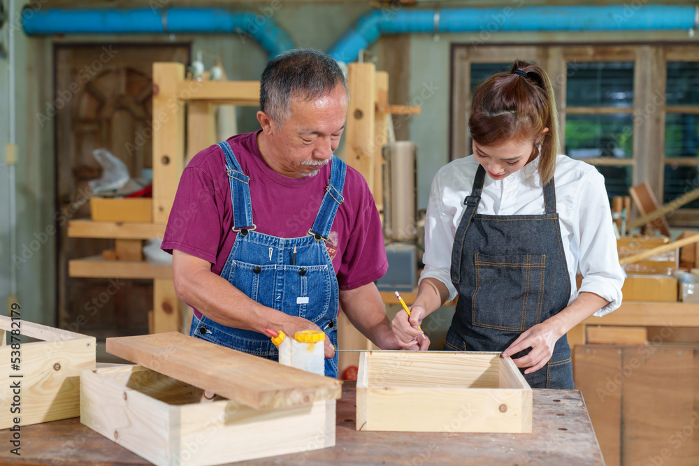 A tutor with a Female carpenter student in a workshop studying for an apprenticeship at a college using a tape measure. A tutor with a Female carpenter student in a workshop studying for an apprenticeship at a college using a tape measure.