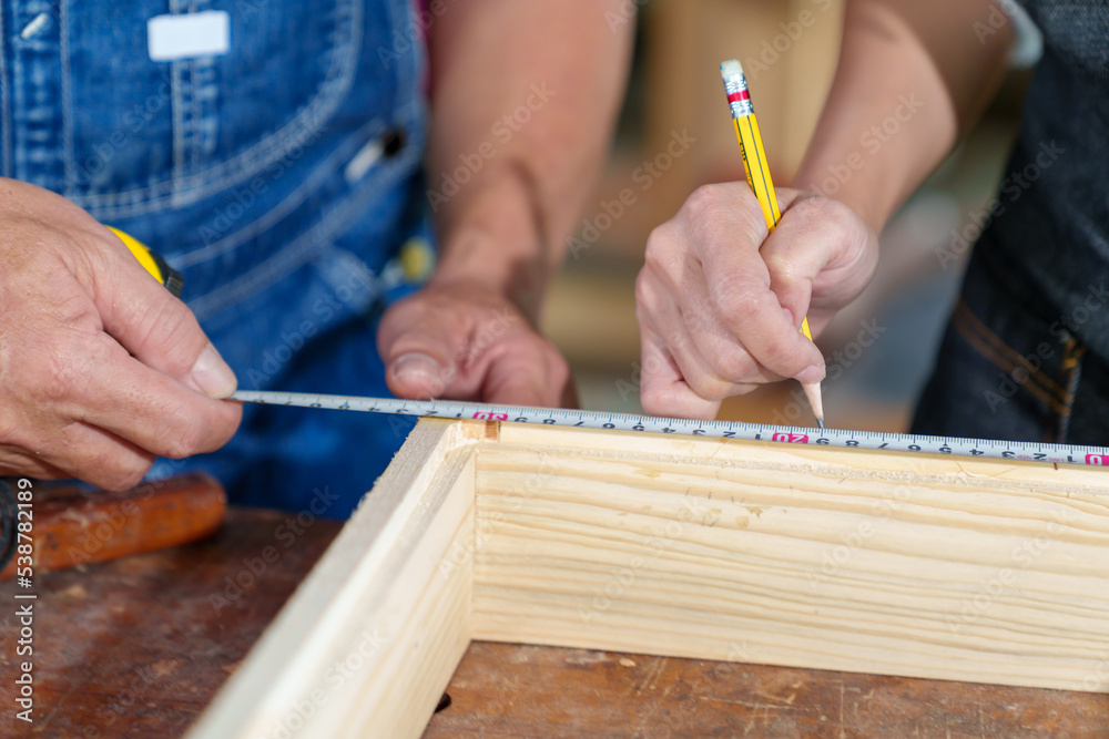 Obraz premium A tutor with a Female carpenter student in a workshop studying for an apprenticeship at a college using a tape measure.