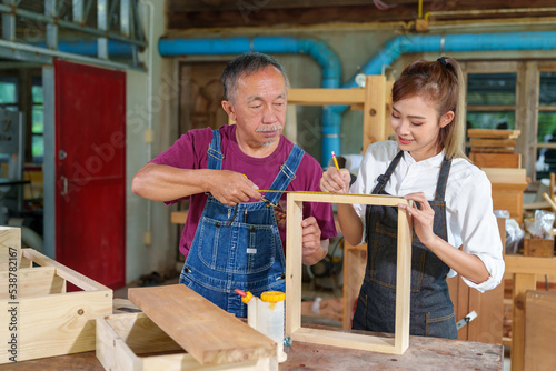 A tutor with a Female carpenter student in a workshop studying for an apprenticeship at a college using a tape measure.