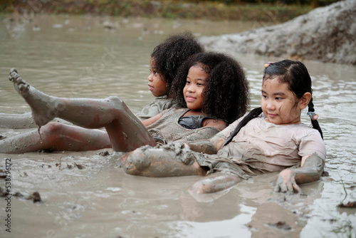 Group of happy children girl playing in wet mud puddle during raining in rainy season.