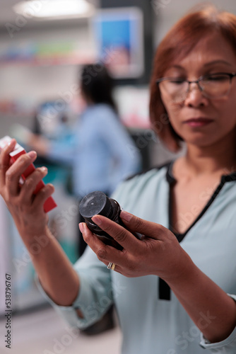 фотографія Female client being indecisive about medicaments, looking at box of cardiology drugs and bottle of sleeping pills