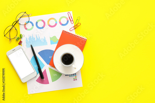 Business charts, mobile phone and stationery on yellow background