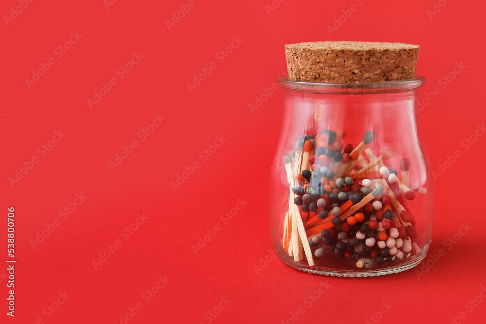 Glass jar with different colorful matches on red background Glass jar with different colorful matches on red background