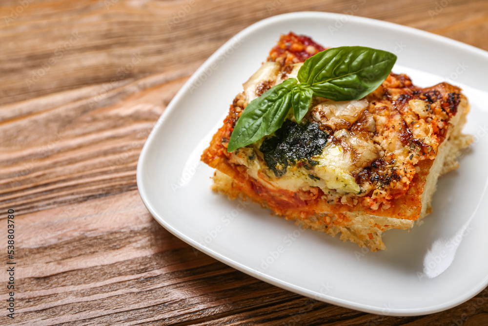 Plate with tasty Italian pie with mozzarella and pesto sauce on wooden background, closeup