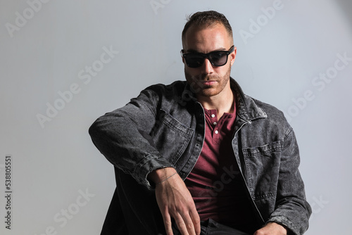seated young guy with sunglasses holding elbow on knee and posing