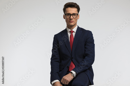 elegant young businessman wearing navy blue suit sitting and posing