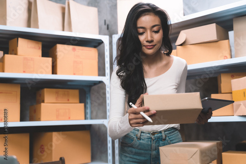 young beautiful woman watching and checking the online order for shipping the parcel to customer drinking a coffee. Young women with new business about online shopping in home office and small store.