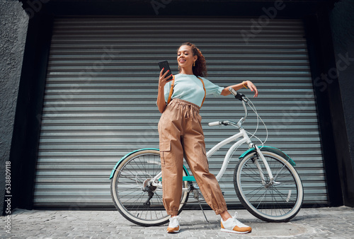 Bicycle, phone and black woman in city, street or urban road outdoors. Bike, travel and happy female from South Africa on 5g mobile tech, internet browsing or social media, web or online surfing.
