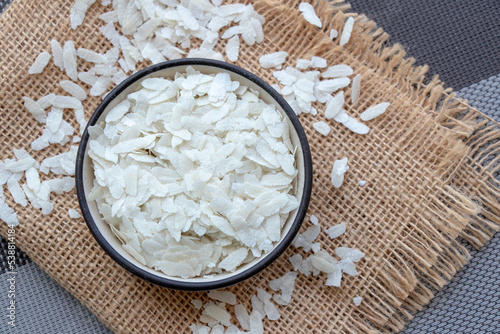 Flattened rice or beaten rice inside of carmic bowl, use in brakefast indian recipe poho over jute mat