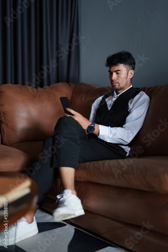Portrait of a good looking and discreet Asian man sitting on the sofa playing on the phone