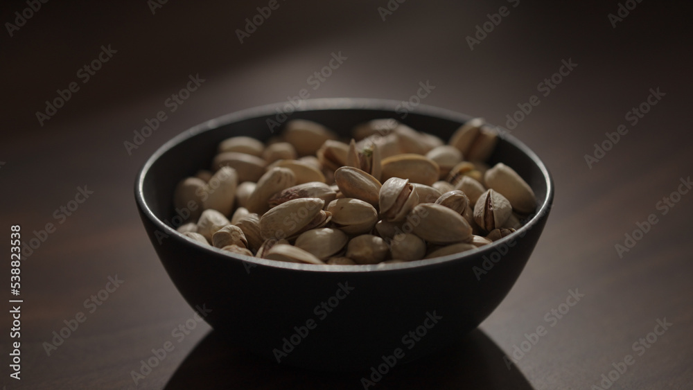 roasted pistachios in black bowl on walnut table roasted pistachios in black bowl on walnut table