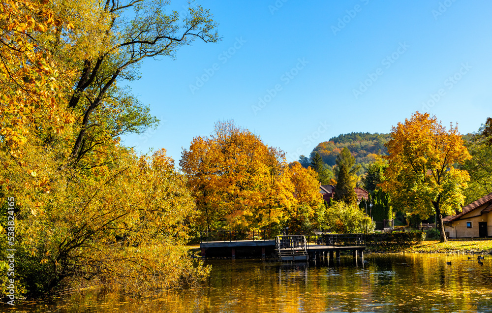 City park and lake with colorful fall trees leaf mosaic in historic old town quarter of Andrychow with Beskidy Mountains in background in Lesser Poland