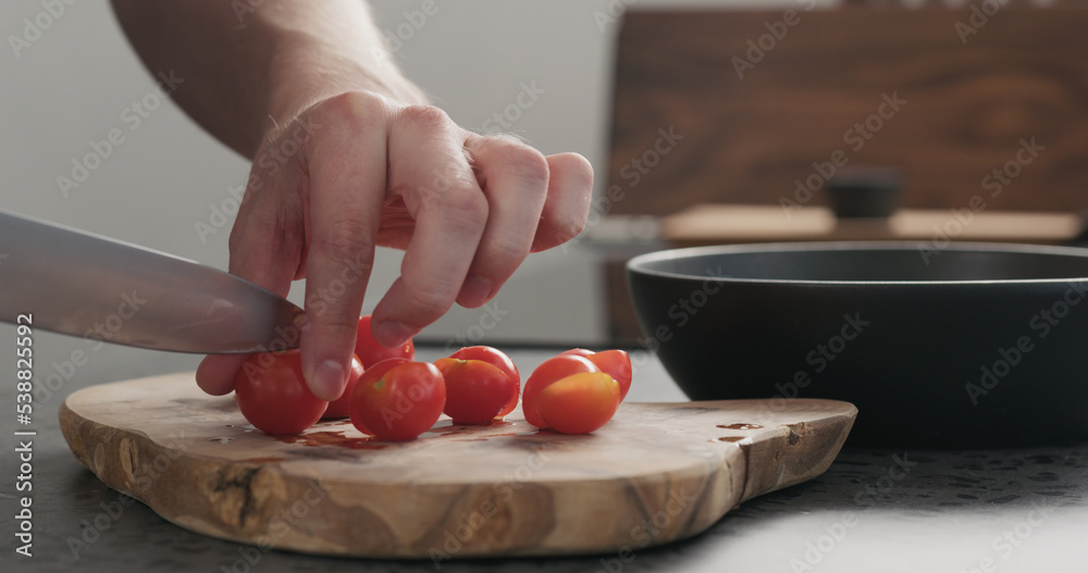 man cuts red cherry tomatoes on olive wood board