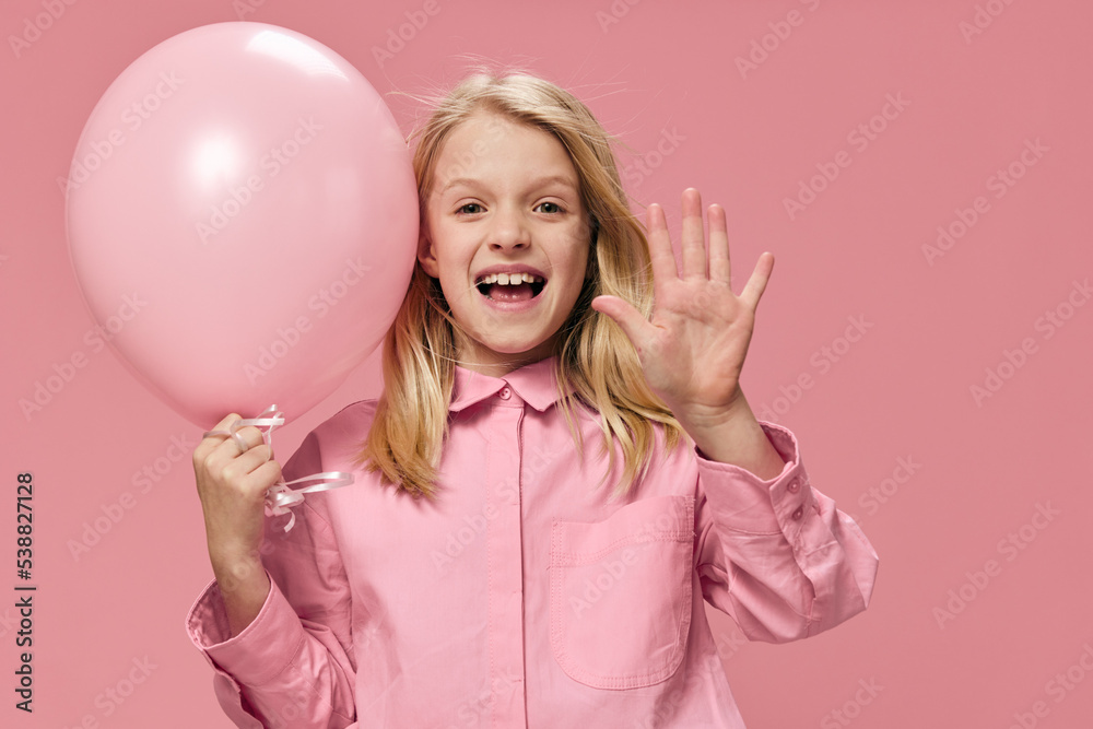 happy, beautiful girl of school age, blonde, stands in a pink shirt with an inflatable pink ball in her hand and smiles broadly, showing five fingers at the camera happy, beautiful girl of school age, blonde, stands in a pink shirt with an inflatable pink ball in her hand and smiles broadly, showing five fingers at the camera