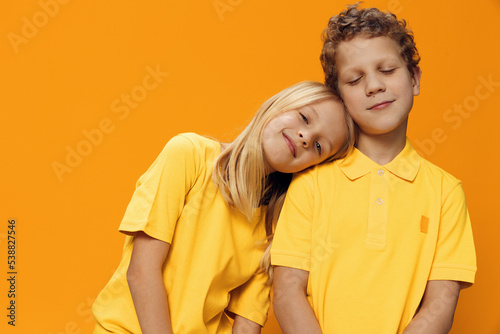 cute, beautiful children, a boy and a girl, stand on a yellow background in yellow clothes, and the girl puts her head on her brother's shoulder. Friendship between children © Tatiana
