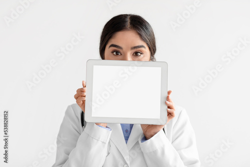 Young hindu lady doctor in coat show tablet with blank screen, isolated on white background