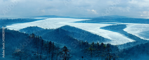 blue ice and cracks on the surface of the ice  frozen lake  forest on background