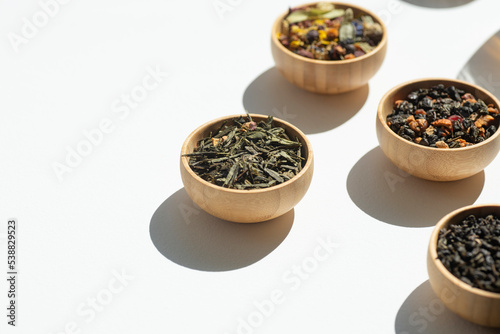 Different types of green, black and herbal tea in a wooden bowl. Variety of dry leaves and flowers. Organic high-quality ingredients for a drink. Soft focus on one bowl photo