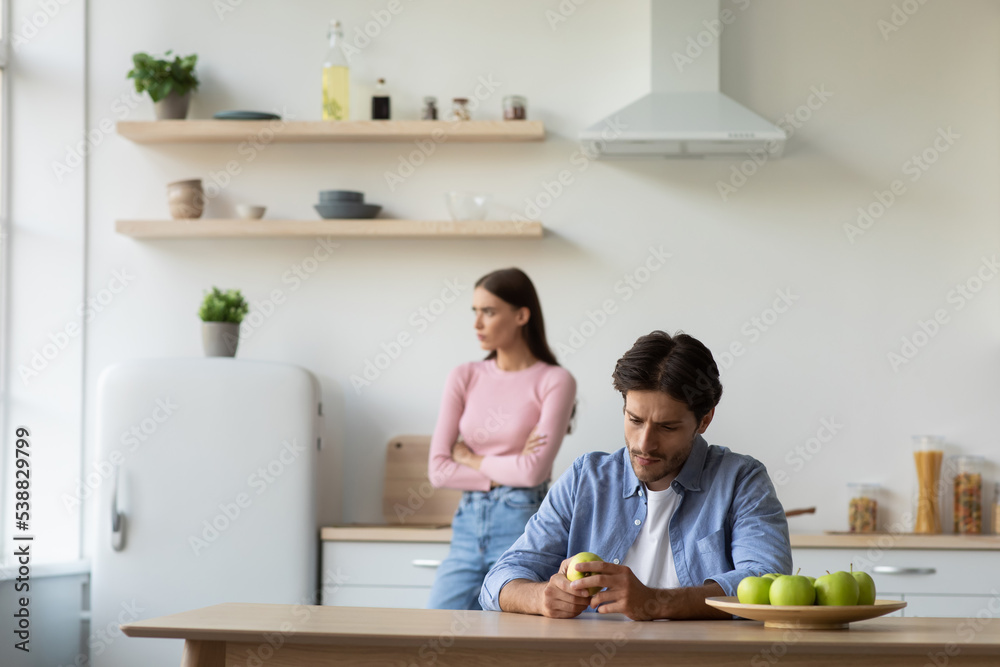 Upset offended millennial caucasian husband ignores depressed unhappy wife after quarrel in white kitchen interior Upset offended millennial caucasian husband ignores depressed unhappy wife after quarrel in white kitchen interior
