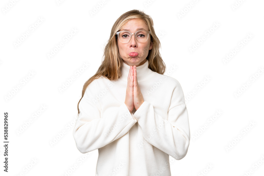 Young blonde woman over isolated background keeps palm together. Person asks for something Young blonde woman over isolated background keeps palm together. Person asks for something
