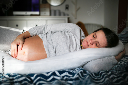 Middle-aged pregnant woman sleeps on special pillow for pregnant women in bedroom.