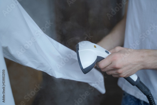 Cropped photo of man using steamer neatly ironing white shirt while holding long sleeve