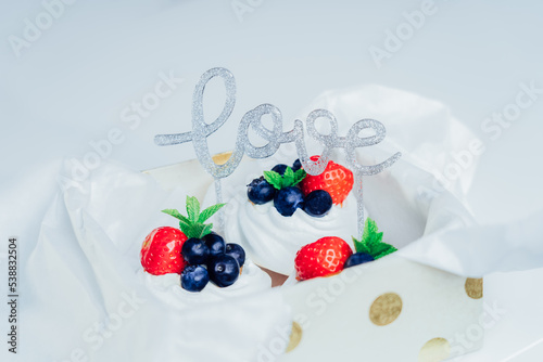 Set of Pavlova meringue dessert nest cakes with fresh strawberries and blueberries packed in gift box with Love word decor. Sweet present for Valentine' s day. made-to-order dessert. Selective focus. photo